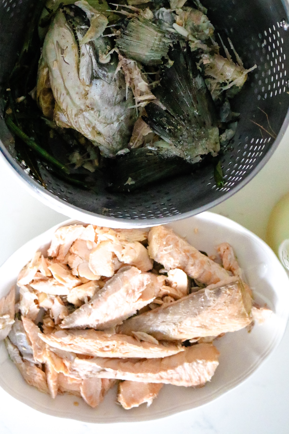 fish cleaned from bones in white bowl next to steal strainer filled with bones and skin