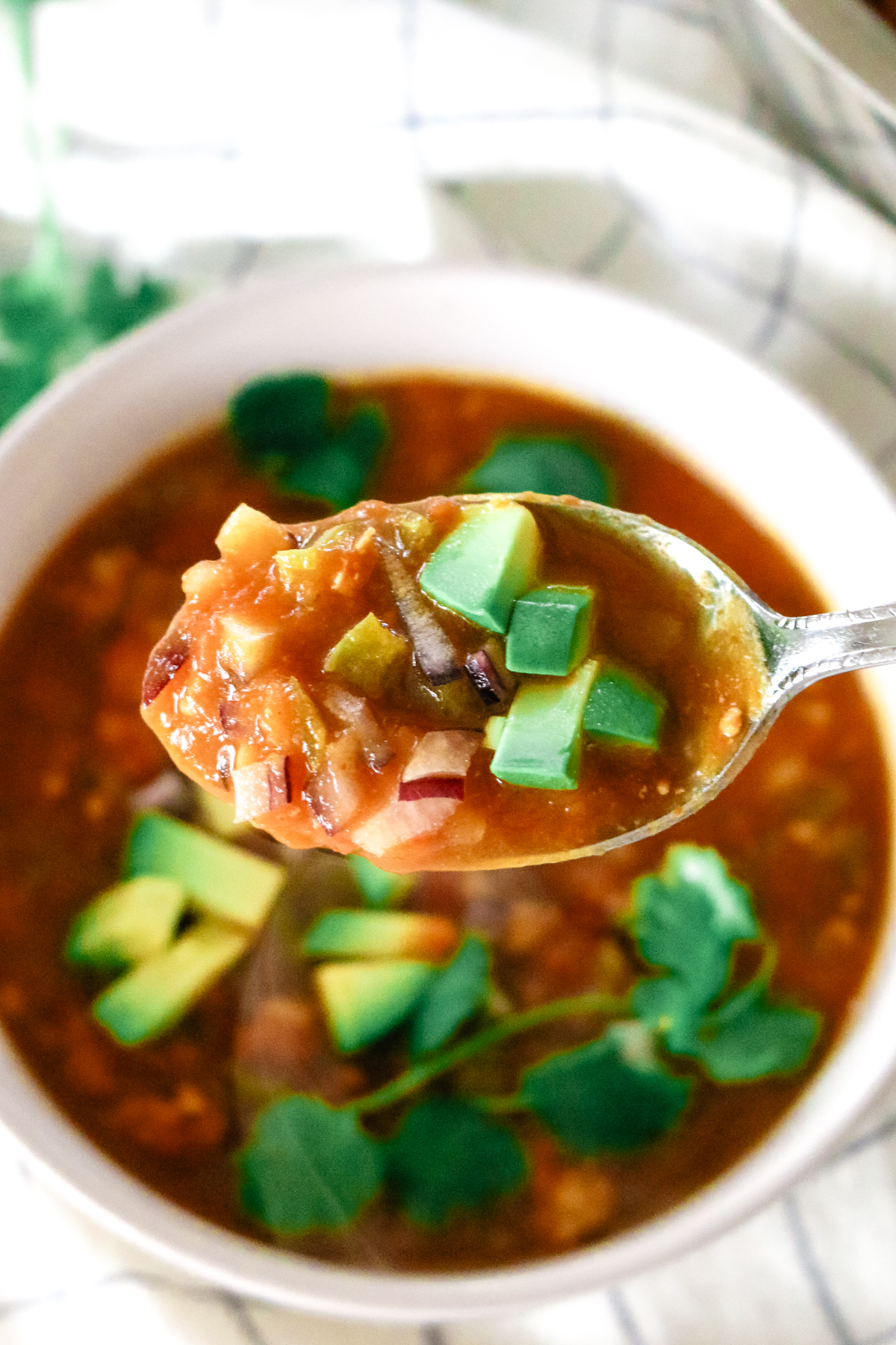 a spoonful of pumpkin turkey chili with diced avocados and red onions as garnish.