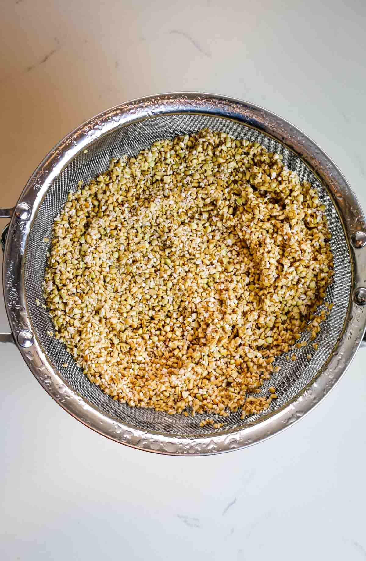 oats and other ingredients in a metal strainer on a white counter