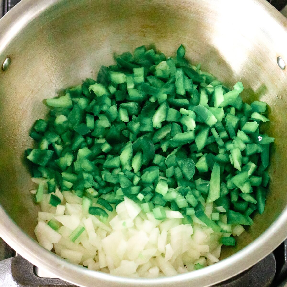 a stainless steel pot with diced onions and bell peppers.