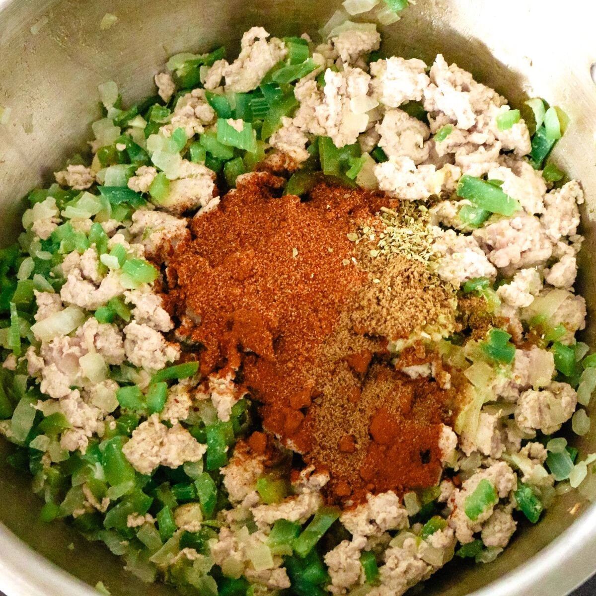a stainless steel pot with ground turkey, peppers, and seasonings.
