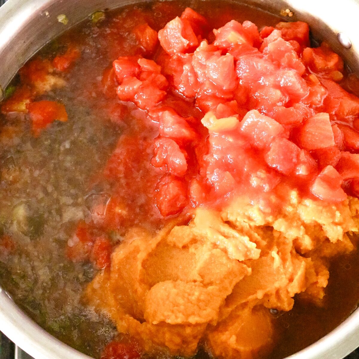a pot with broth, diced tomatoes, and pumpkin puree added to it.