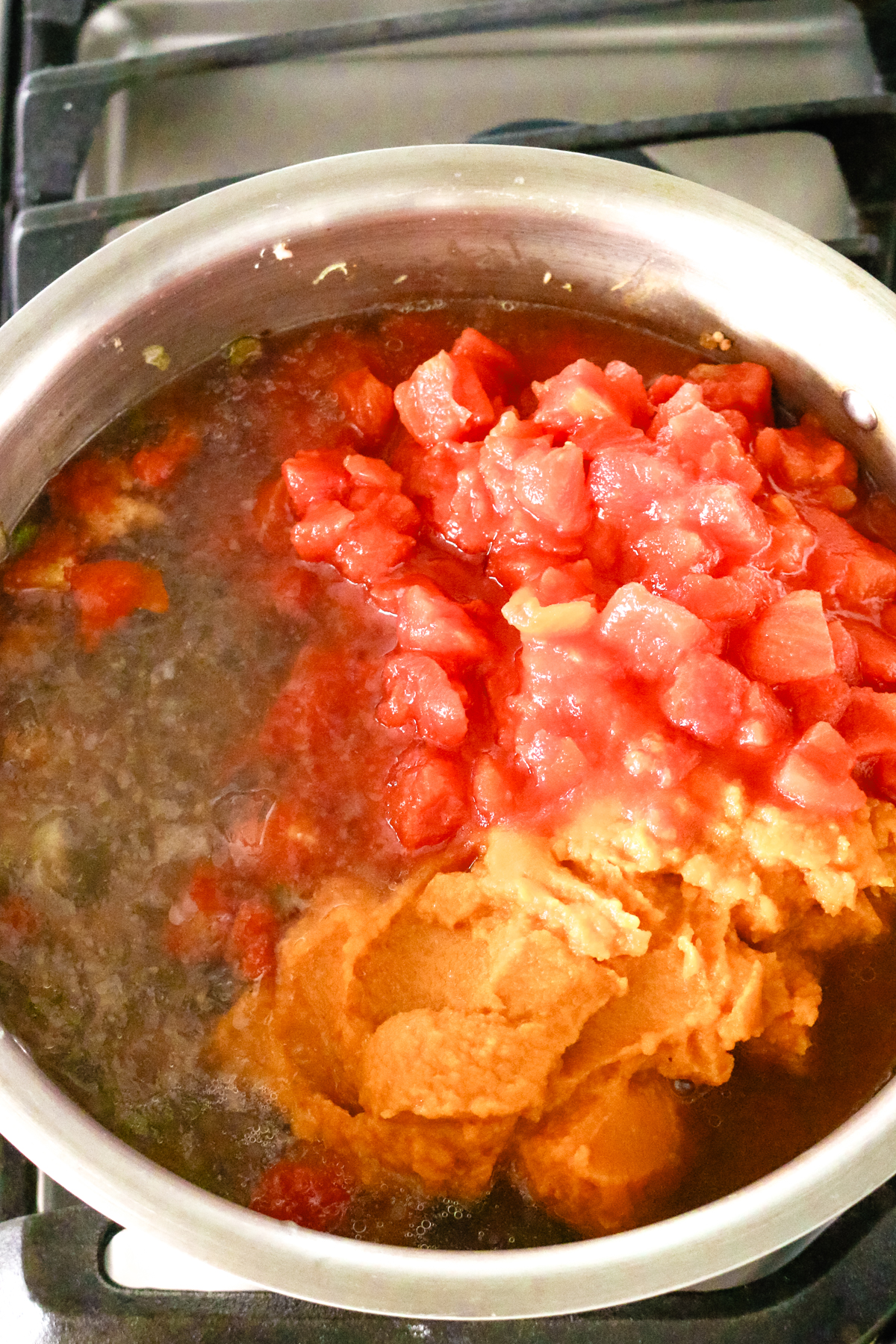 a pot with broth, diced tomatoes, and pumpkin puree added to it.