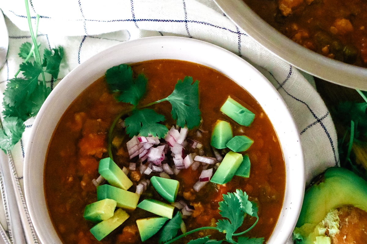 a white bowl full of pumpkin turkey chili with red onions and avocado.