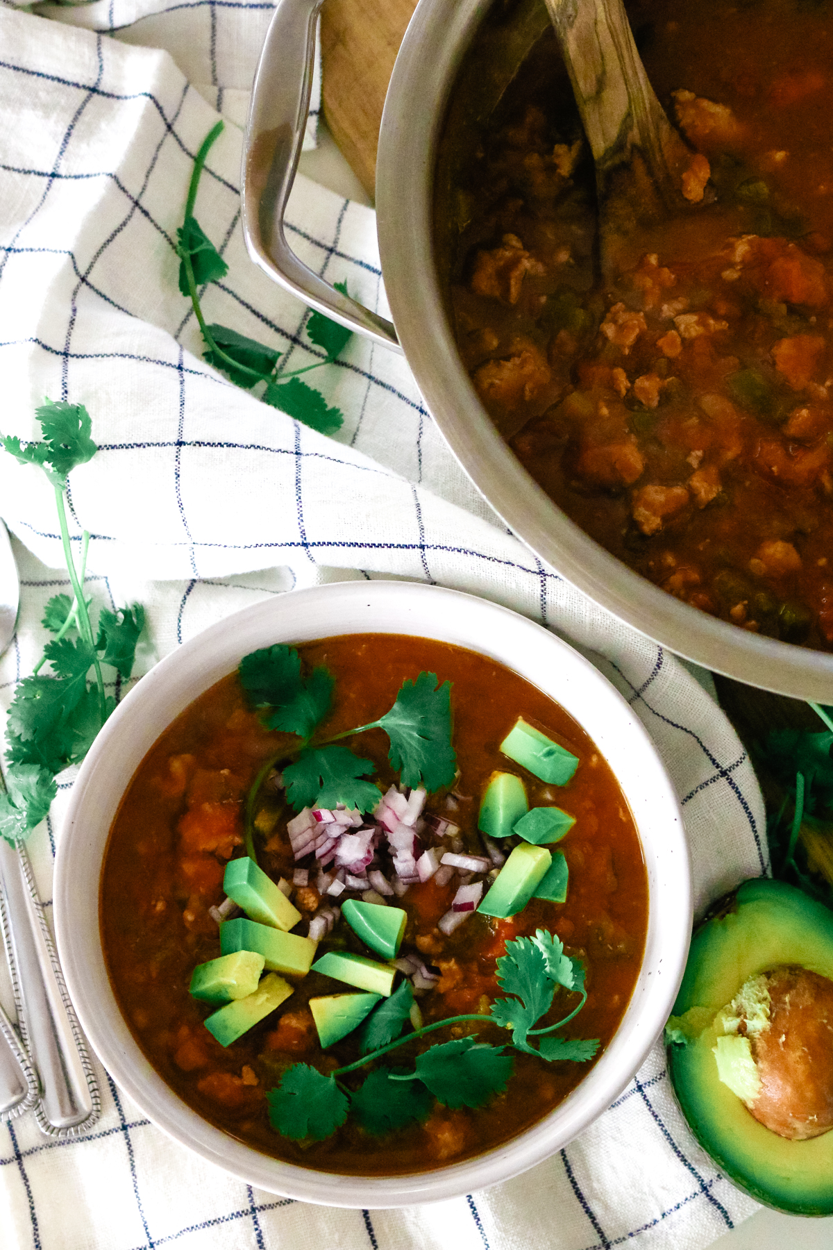 a bowl of pumpkin turkey chili and a large pot to the side with a wooden ladle.