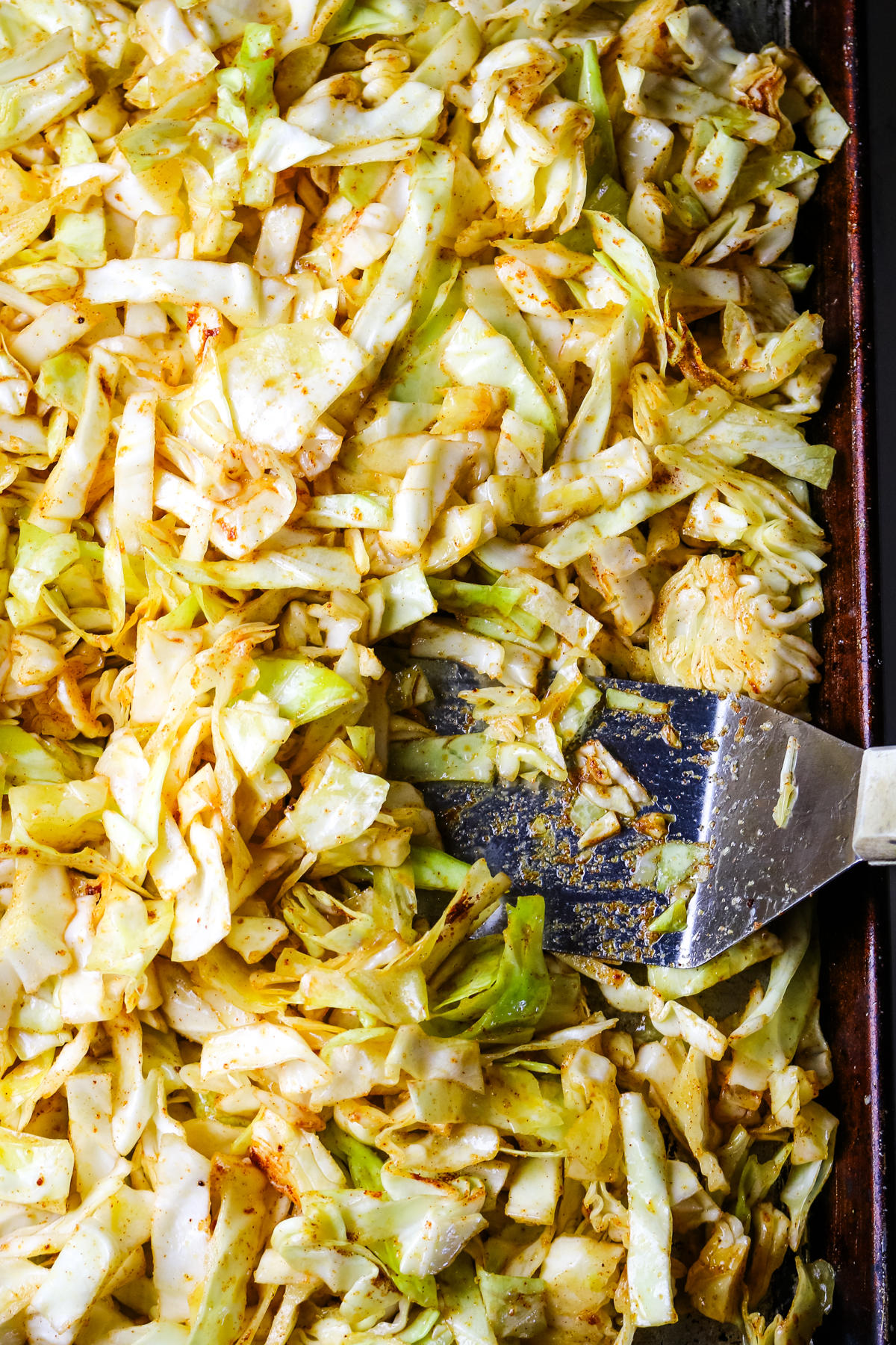 seasoned cabbage on a sheet pan with a wide spatula.