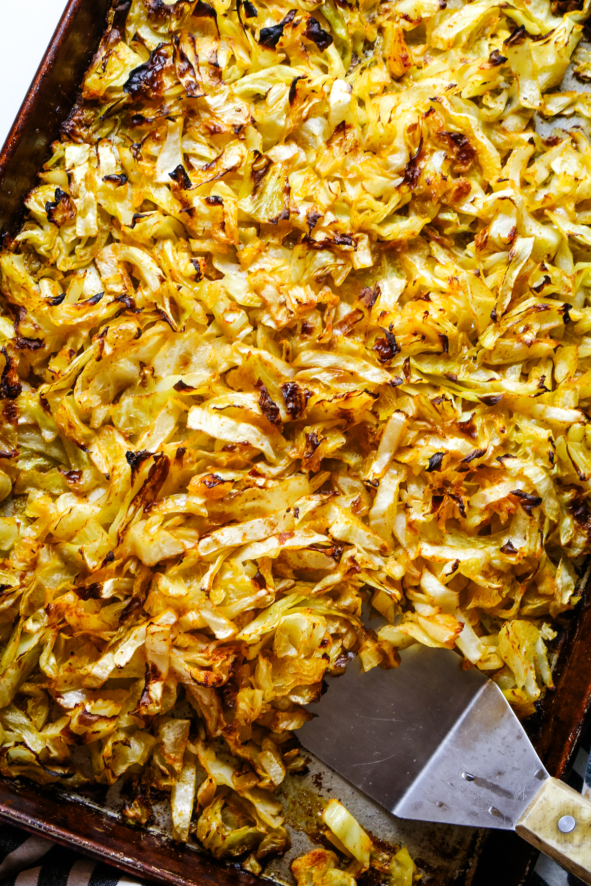 roasted cabbage strips on a sheet pan with a wide ladle.