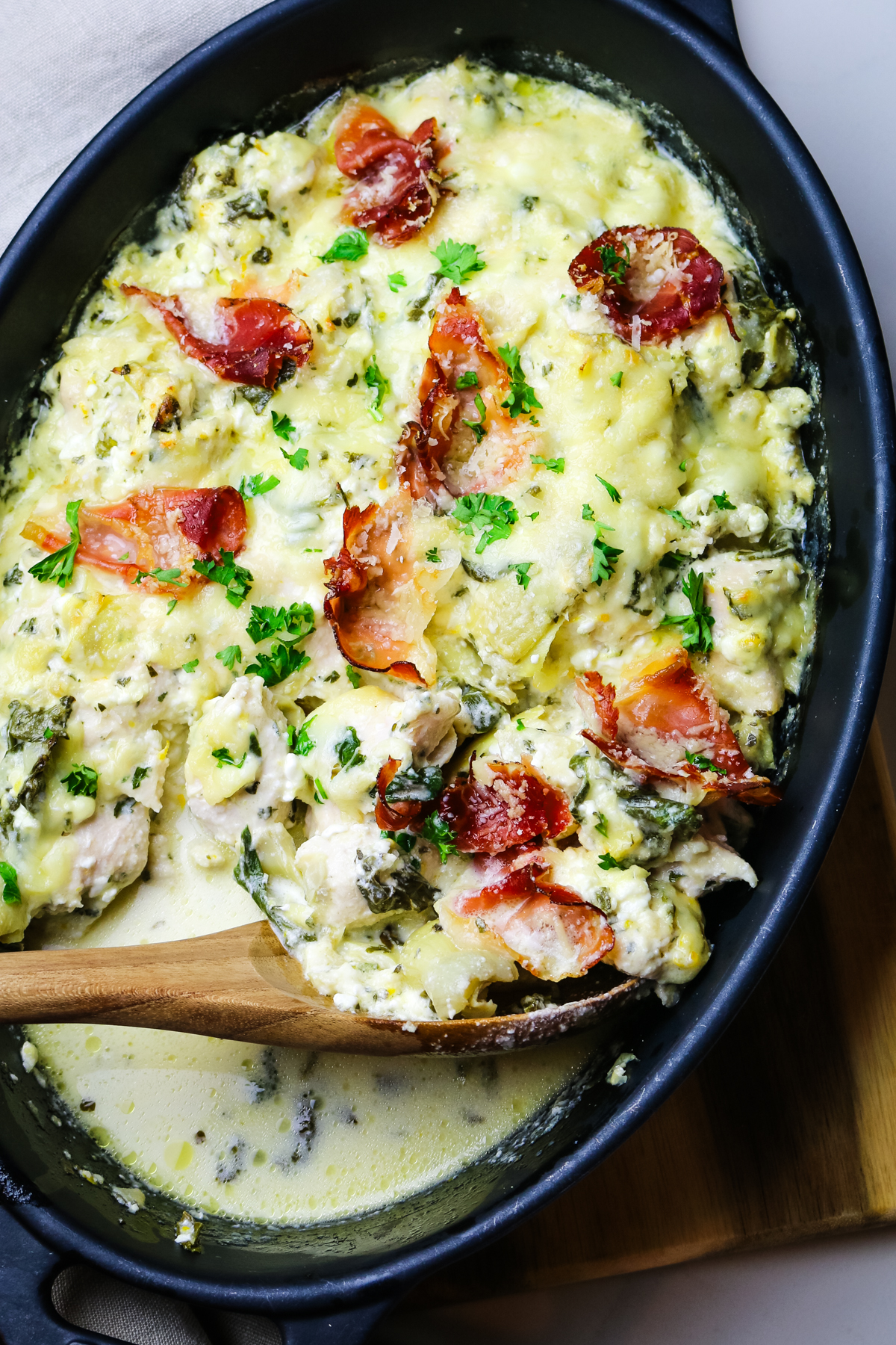 chicken artichoke casserole in black baking dish with prosciutto pieces on top with green parsley.