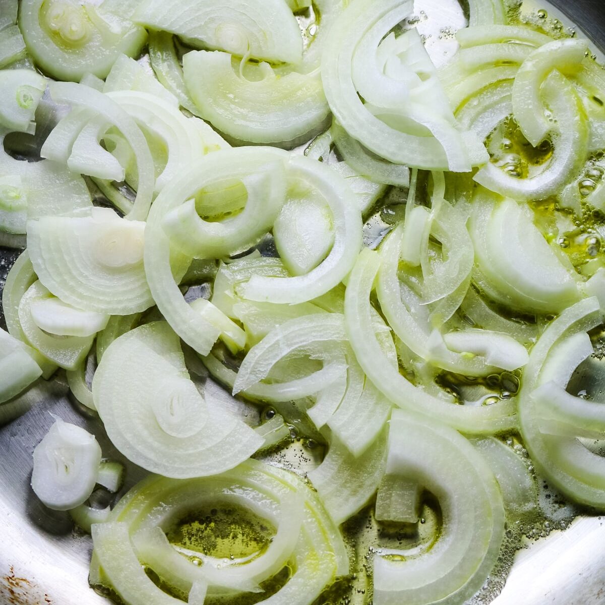 sliced onions added to stainless steel skillet.