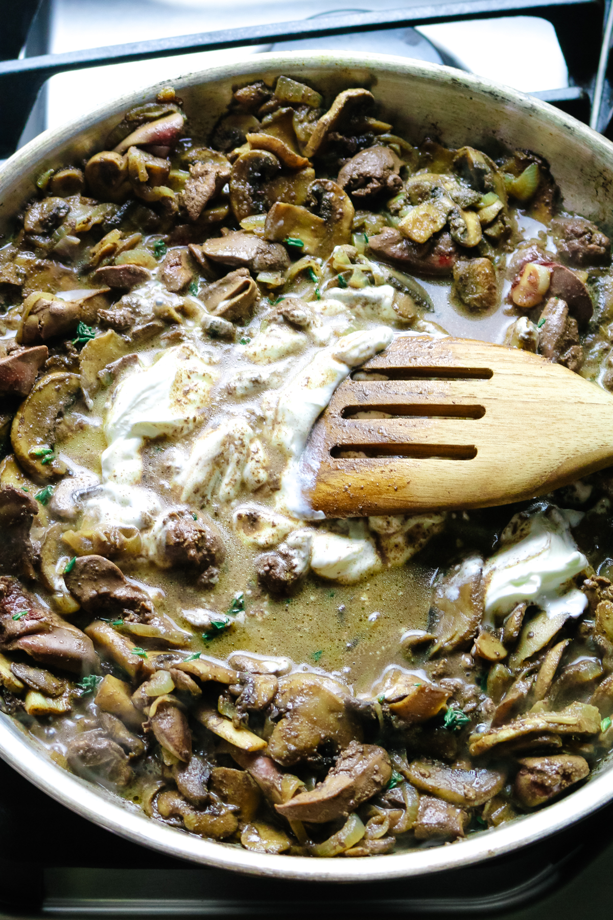 sour cream added to mushrooms and liver in a skillet with wooden spatula.