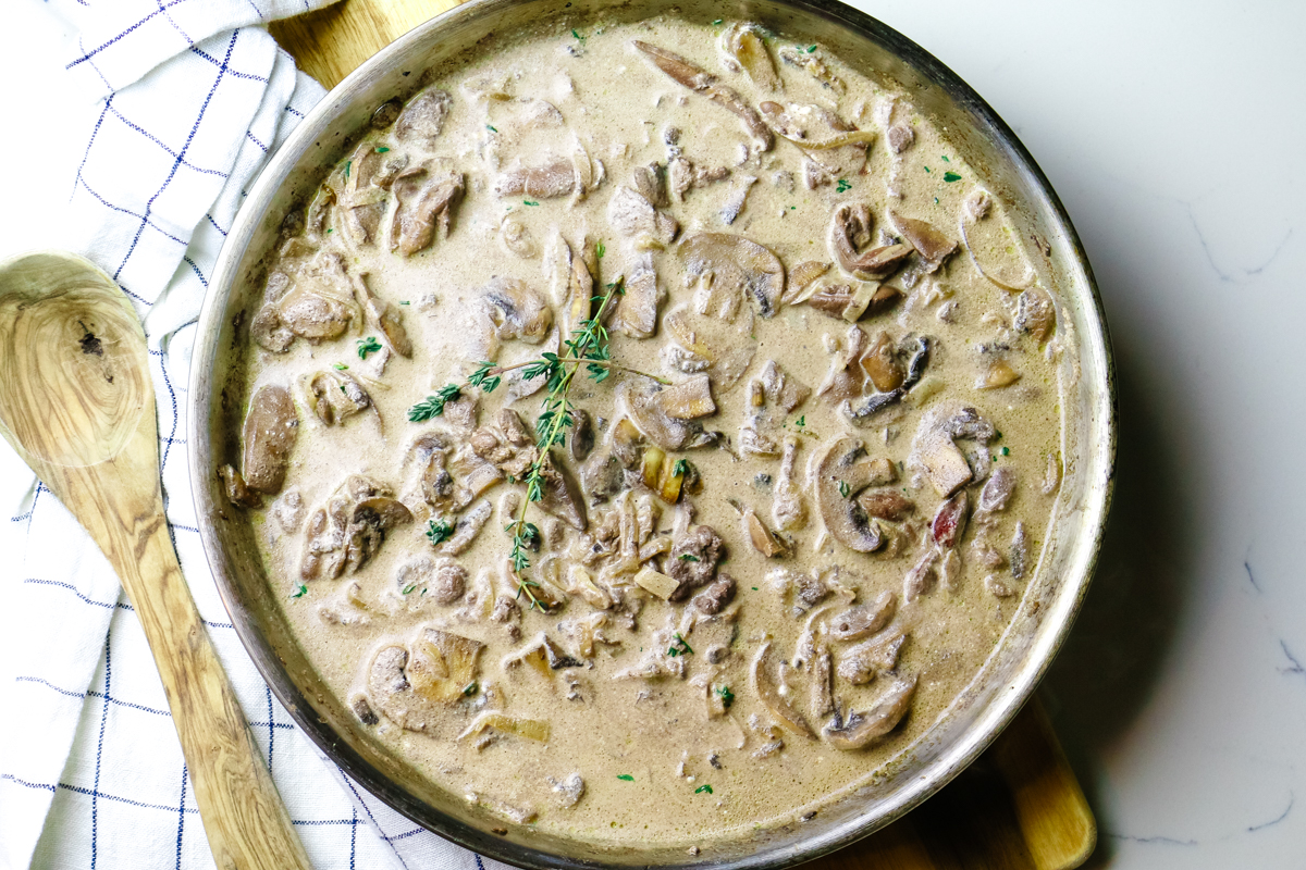 mushrooms and chicken livers in a creamy sauce in a stainless steel skillet with wooden spoon.