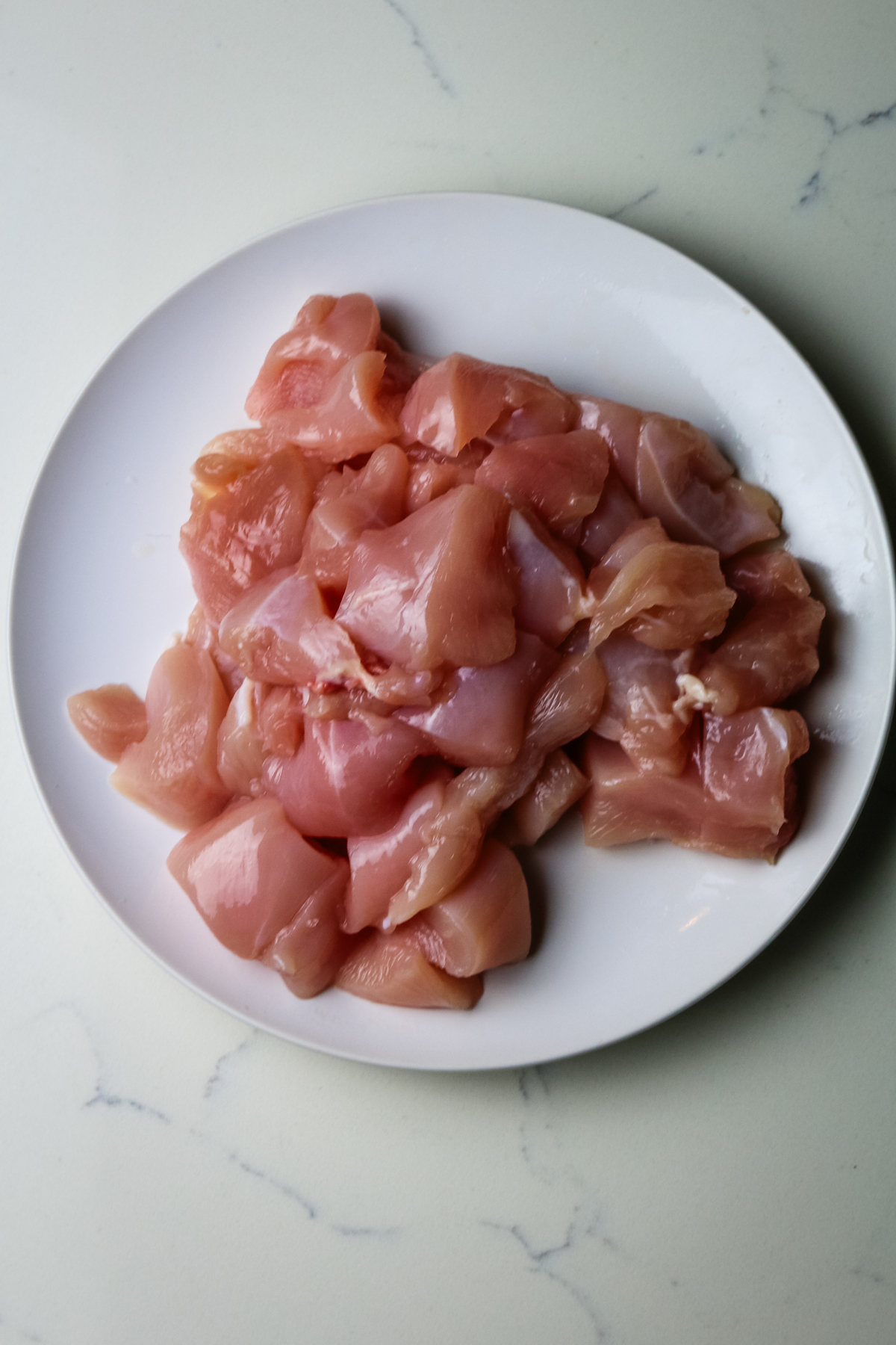 cubed raw chicken on a white plate.