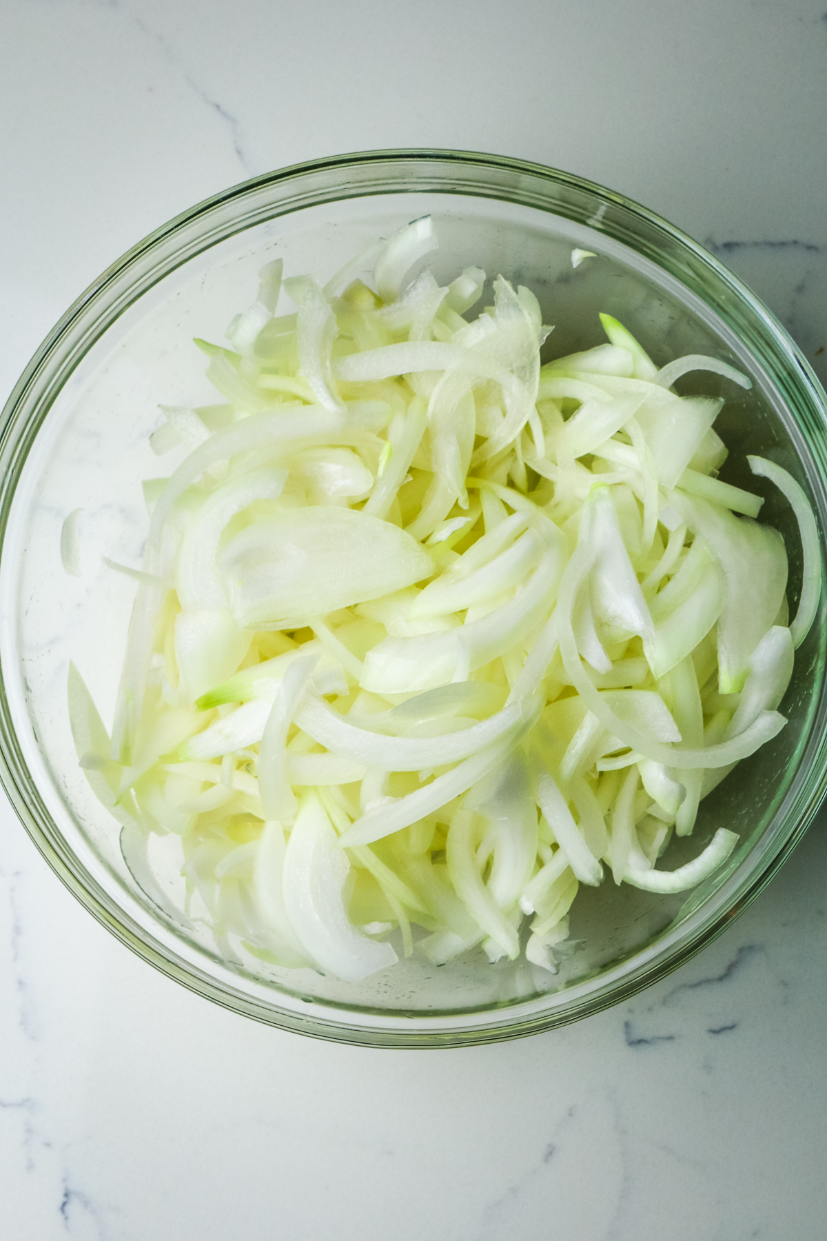 thinly sliced yellow onion in a glass bowl.