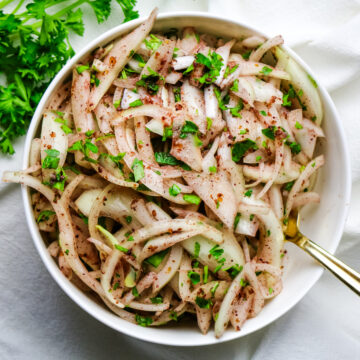 sliced onions in a white bowl with sumac seasoning and parsley.