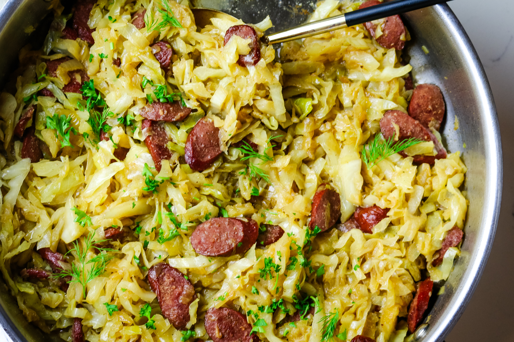 cabbage with polish sausage fried in a pan with fresh herbs garnished.