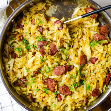 fried cabbage and sausage with dill and fresh parsley garnish in a skillet.