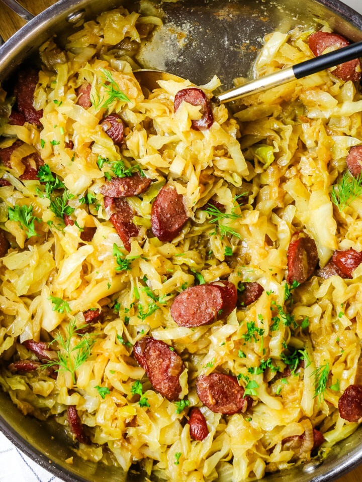 fried cabbage and sausage with dill and fresh parsley garnish in a skillet.