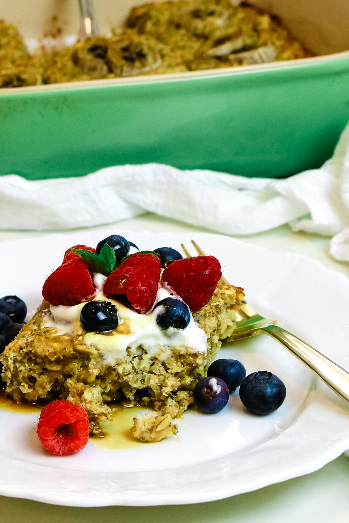 a slice of baked protein oats on a white plate with baking dish in background and fresh berries on top.
