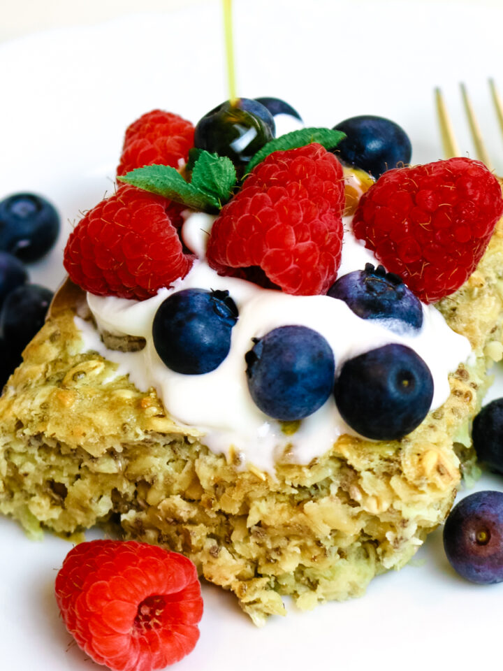 baked oats on a white plate with fresh berries and whipped cream and maple syrup drizzle.
