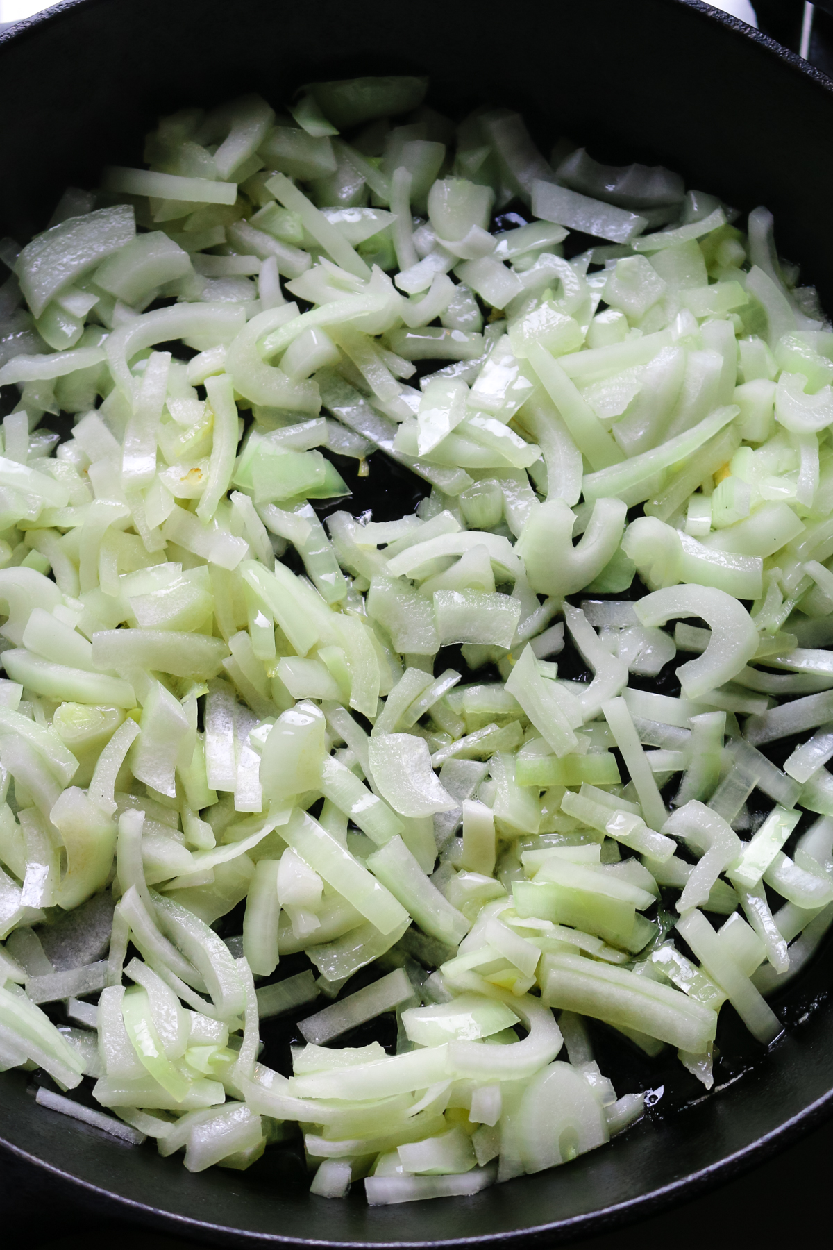 sliced onions in a cast iron skillet being sauteed.