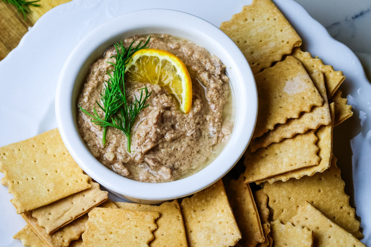 cod liver pate in a small ramekin with fresh dill and lemon slice and crackers.