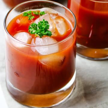 tomato juice in a small glass with ice cubes and parsley sprig.