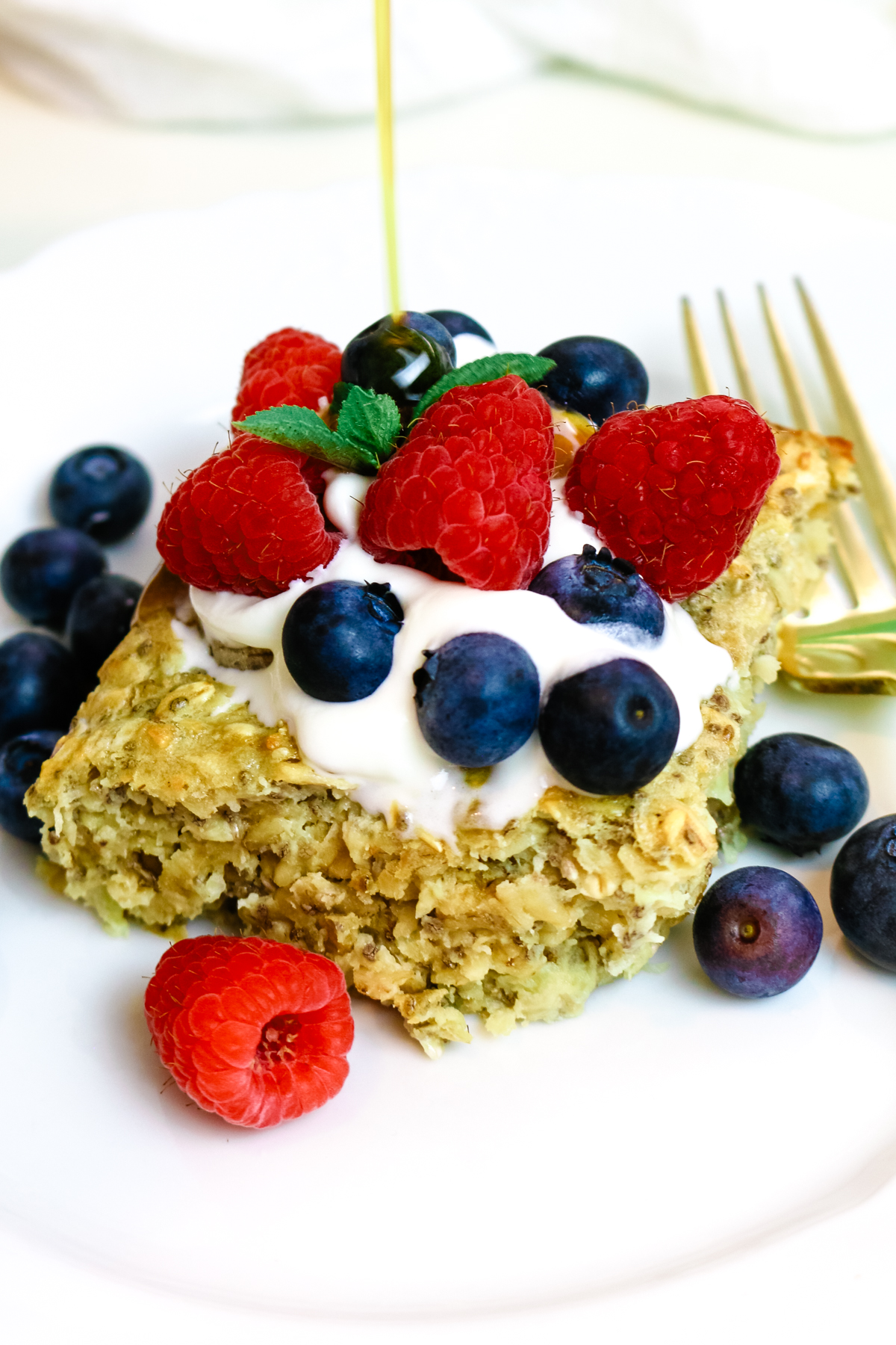 slice of baked oats on a white plate with a fork on the side and fresh berry topping.