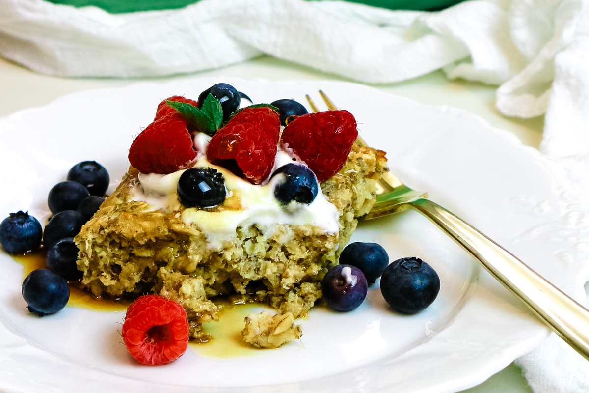 protein baked oats on a white plate with fresh berries and whipped cream on top.