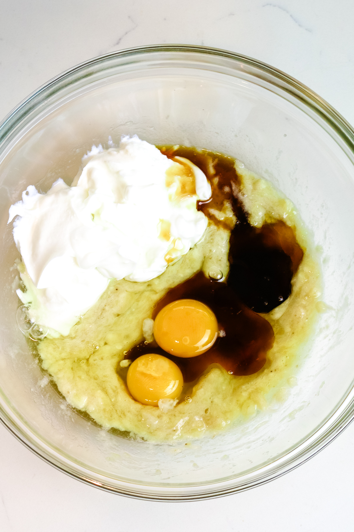 wet ingredients in a large mixing bowl including mashed bananas, protein, eggs, and vanilla.