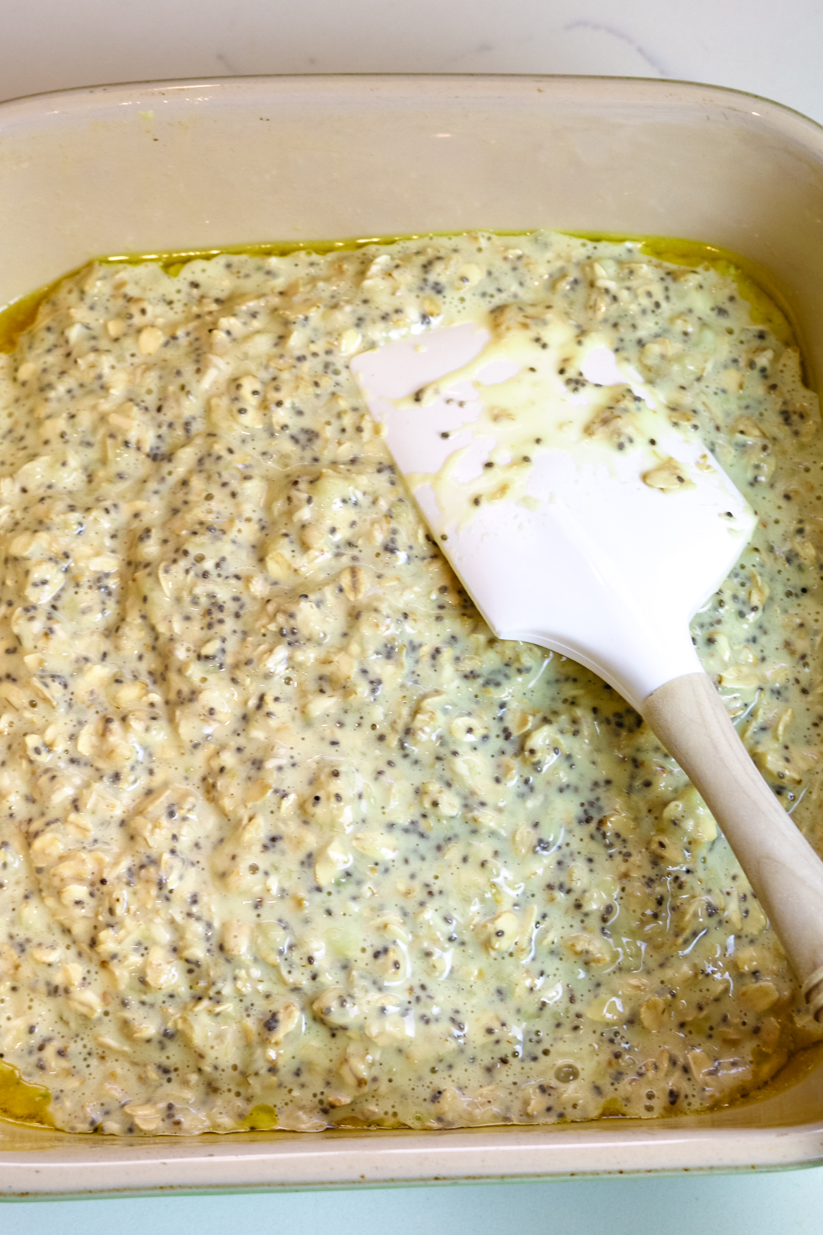 batter with oats, chia seeds, and bananas spread out in a baking dish with a spatula.