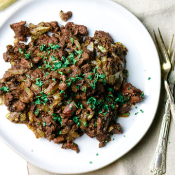 chopped and sauteed liver with onions on a white plate with green parsley garnished.