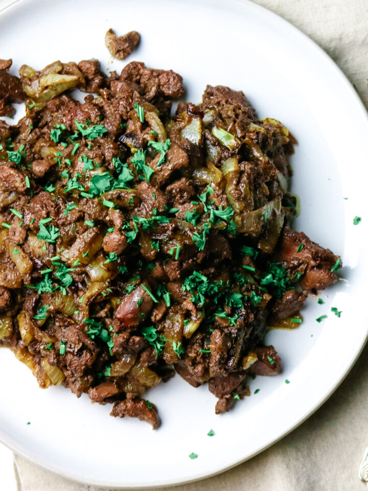 chopped and sauteed liver with onions on a white plate with green parsley garnished.