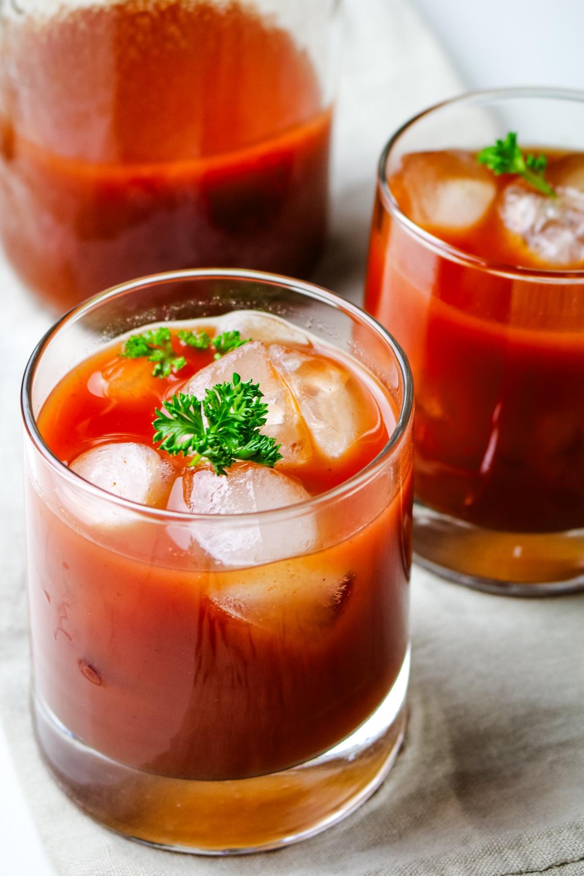 tomato juice in a two glasses with a mason jar with tomato juice in the background.