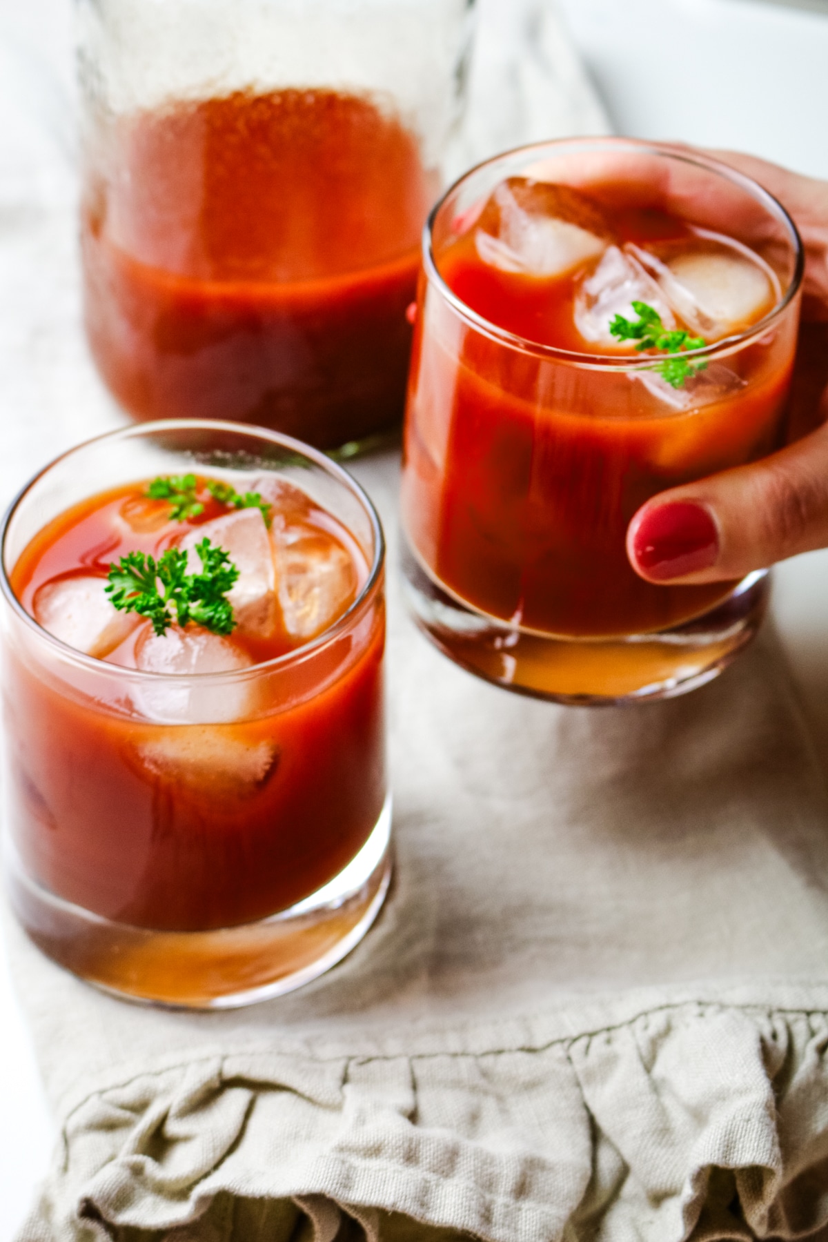tomato juice in 2 glasses with one hand picking up one glass.