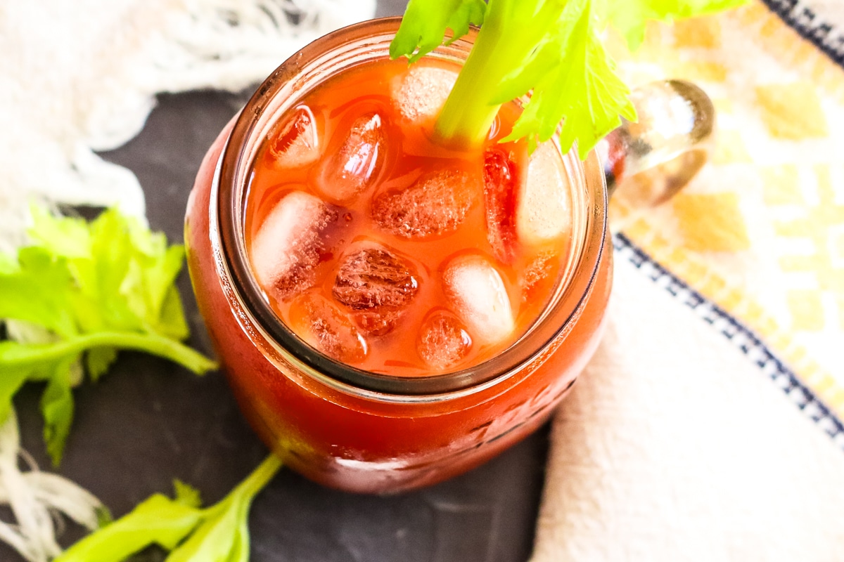 tomato juice with ice cubes in a mason jar with a celery rib.
