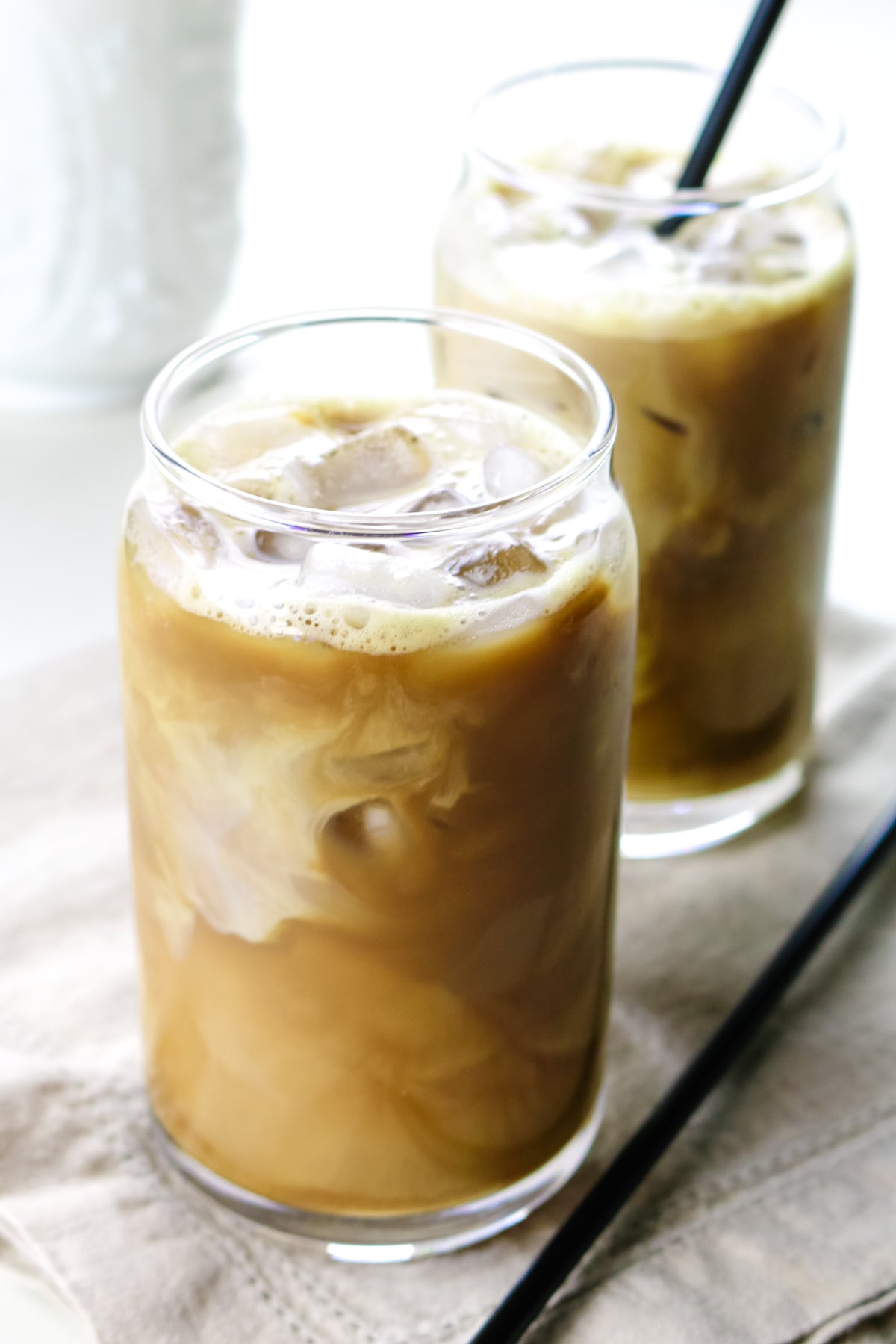 iced coffee with white swirls from milk in a glass on nude linen.