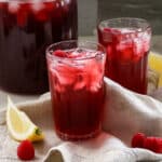 hibiscus tea in glasses with raspberries and lemon wedges.