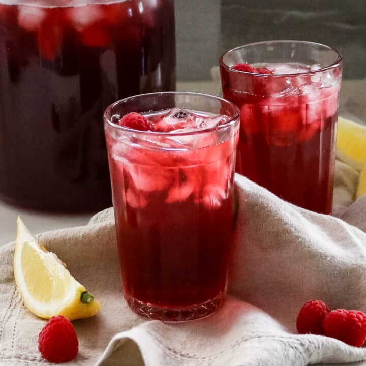 hibiscus tea in glasses with raspberries and lemon wedges.