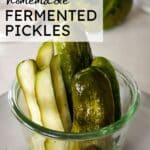 pickle spears in a glass bowl with a jar of pickles in the background.