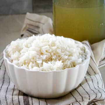 Cooked rice in a white bowl, with bone broth in a clear jar behind it.