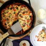 A slice of pizza on a white plate, grated cheese in a clear bowl, and a crustless pizza in a pan on the side.
