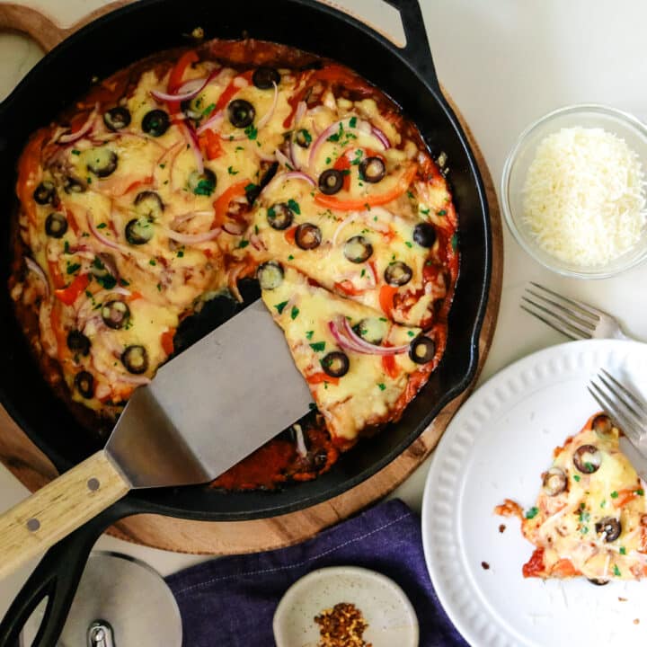 A slice of pizza on a white plate, grated cheese in a clear bowl, and a crustless pizza in a pan on the side.