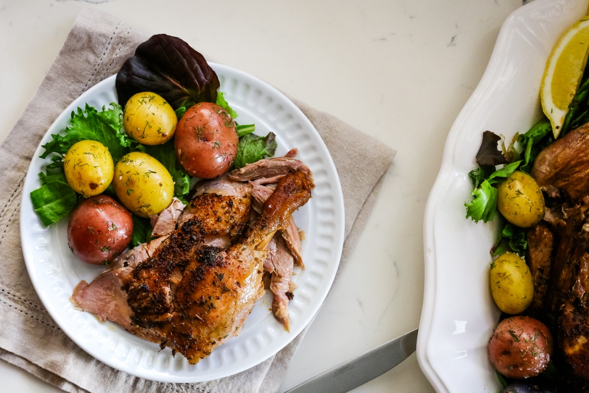 Seasoned quarter leg part of a duck in a white plate with marble potatoes and vegetables.