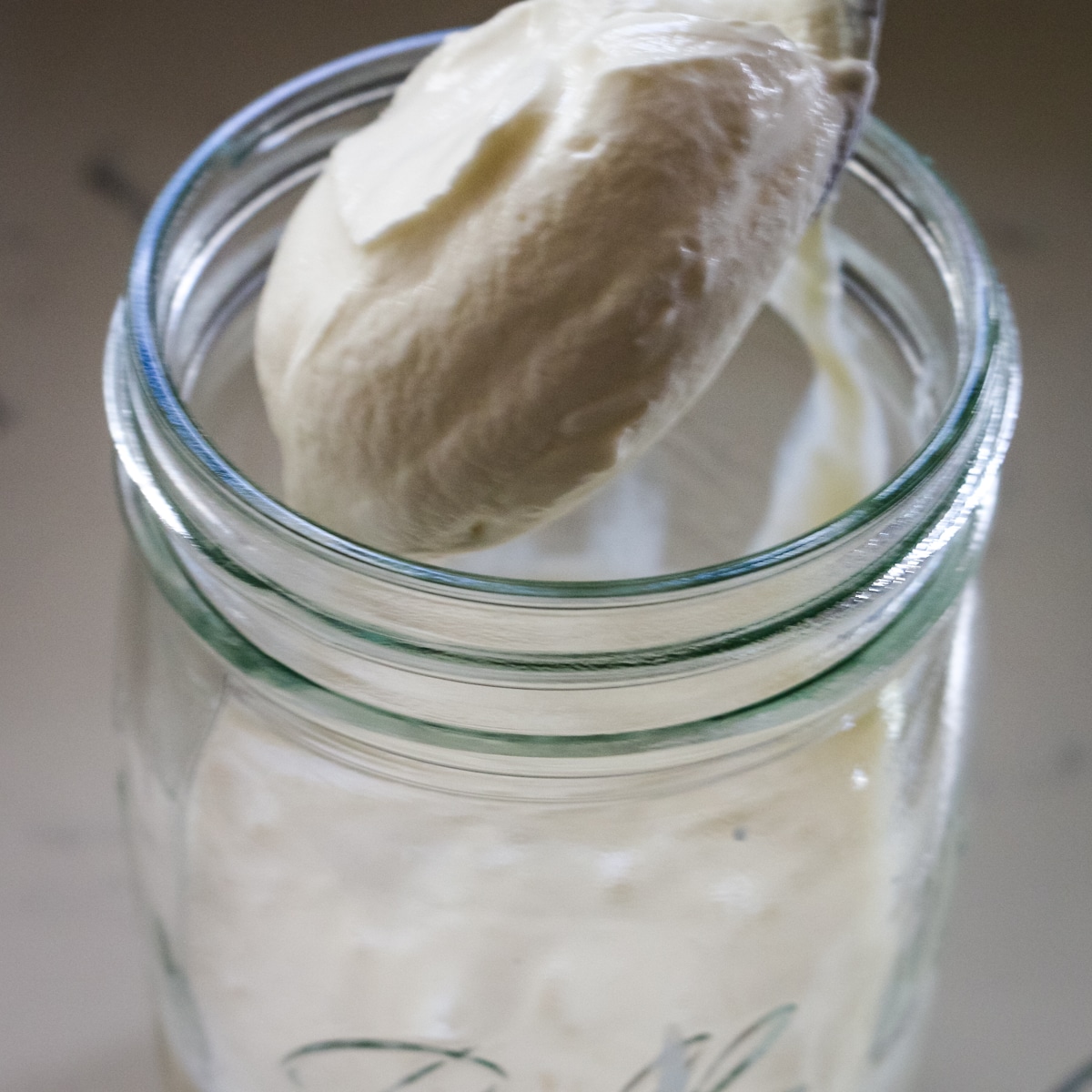 Sour cream in spoon, transferring to a glass jar.