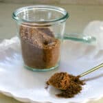 Taco seasoning in a clear glass and on a spoon on a white plate.