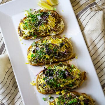 Sardine toast on a white plate, with a lemon on the side.