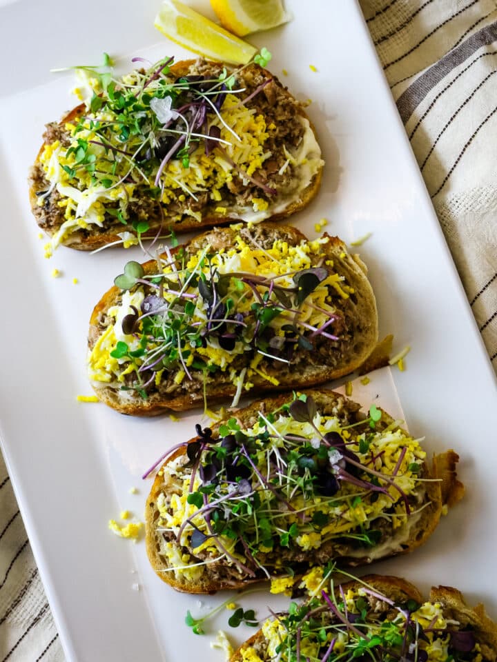 Sardine toast on a white plate, with a lemon on the side.