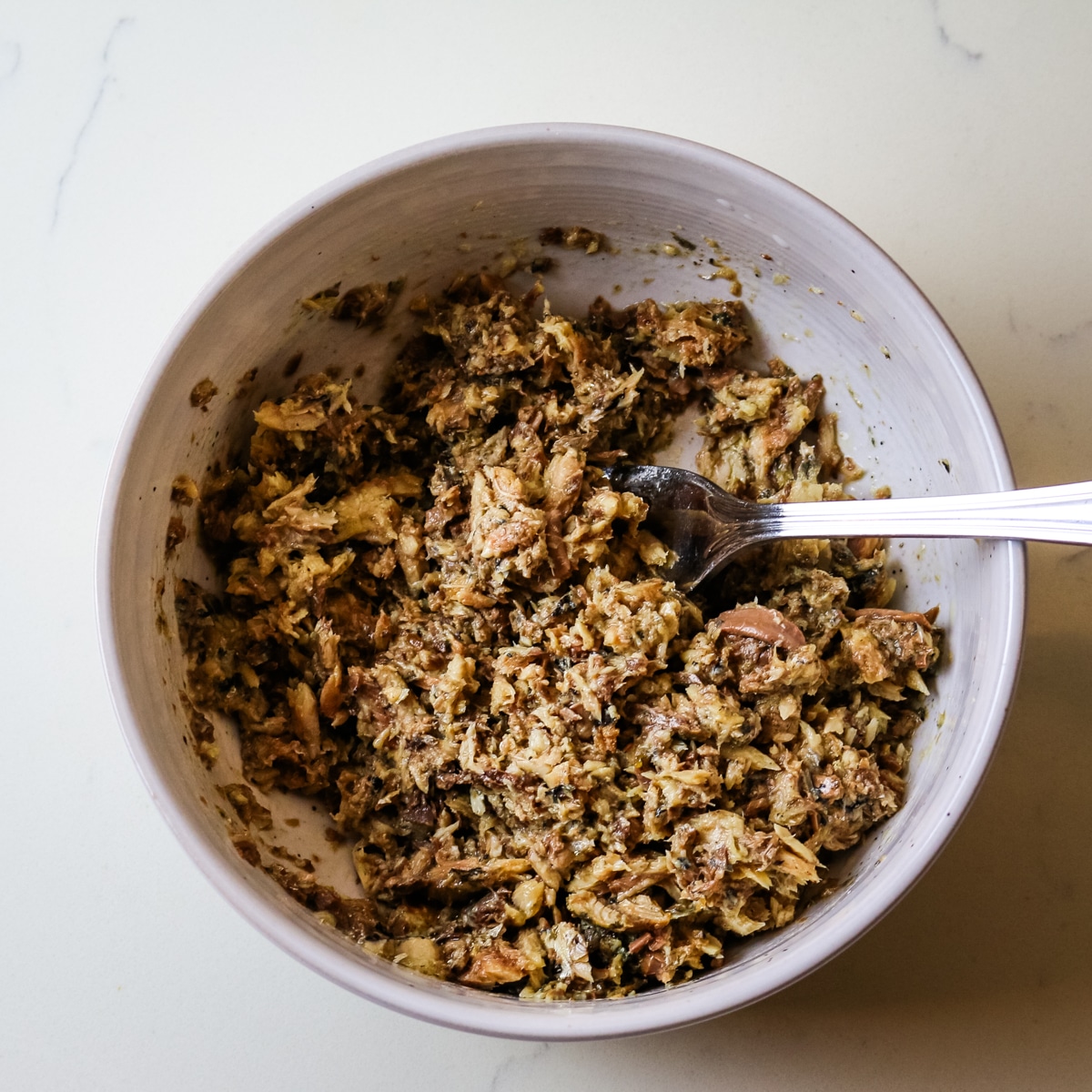 Shredded sardines in a white bowl with a fork in it.