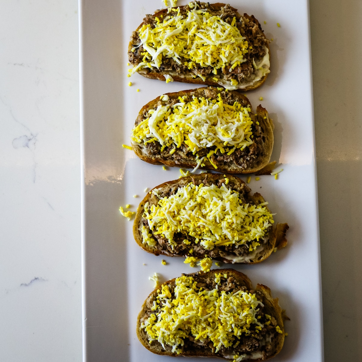 Four pieces of bread with sardines and egg on a white plate.