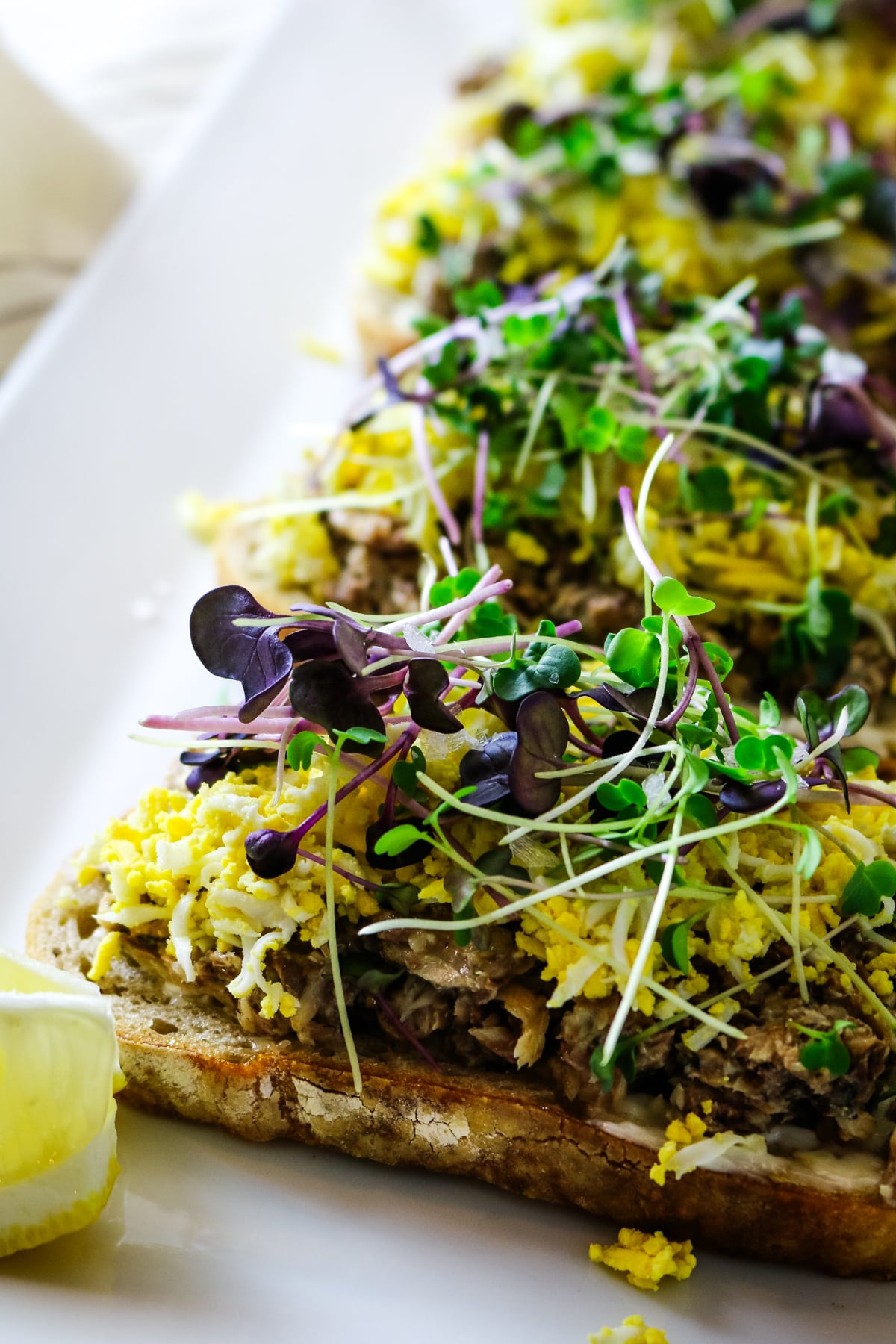 Sardine toast on a white plate, with a lemon on the side.